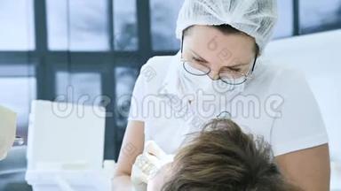 女牙医戴眼镜面罩和白帽检查病人的口腔。 牙医`的工作