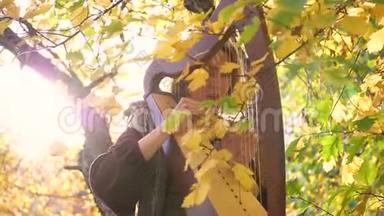 一个年轻的女孩弹竖琴。 她<strong>坐在</strong>秋天公园的一棵<strong>树下</strong>。