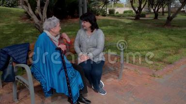 女<strong>志愿者</strong>和老妇人坐<strong>在</strong>城市公园的长椅上谈话