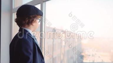 穿着商务服、领带和帽子的小男孩从商务办公室的窗户往外看
