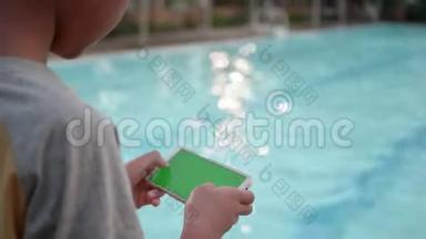 儿童手使用智能手机在线游戏，绿色屏幕放松附近游泳池在晚上。