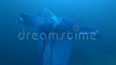 蓝色塑料雨衣作为幽灵慢慢漂浮在蓝色的水中。 海洋的水下塑料污染。 塑料垃圾