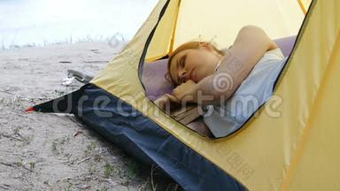 年轻的女旅行者睡在帐篷里。 疲惫的徒步旅行者女孩在露营帐篷里拿着一本书睡着了。 徒步旅行，旅游，绿色