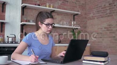 戴眼镜的年轻女子在家里的<strong>笔记</strong>本电脑上工作或学习时在剪贴板上写<strong>笔记</strong>