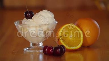 樱桃放在冰淇淋勺上。玻璃碗里有樱桃的冰淇淋，木桌上有橘子。准备