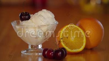 樱桃放在<strong>冰淇淋</strong>勺上。玻璃碗里有樱桃的<strong>冰淇淋</strong>，木桌上有橘子。准备