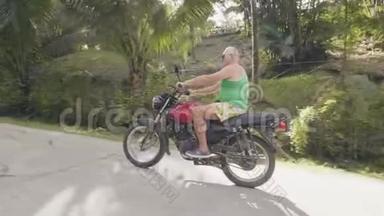 在绿色高地景观热带公路上骑摩托车的成年男子。 一个骑摩托车的退休老人