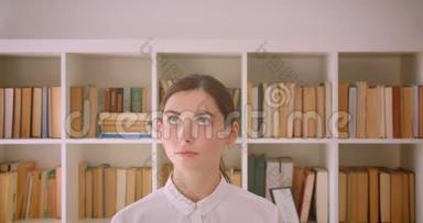 年轻滑稽的白种人女商人的特写镜头，她微笑着站在办公室，书架上放着书架