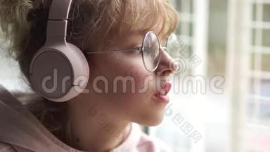 女学生听音乐，很伤心。 窗户边一个戴着粉色耳机眼镜的女孩的肖像