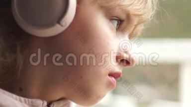 窗户边一个戴着粉红色耳机的女孩的肖像。 女学生听音乐，很伤心