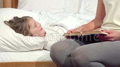 可爱的小女孩在床上大笑，她的母亲在睡觉前给她读了一本书