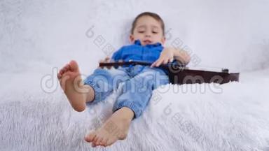 一个拿着吉他的孩子躺在白色的沙发上，摸着吉他的琴弦