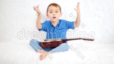 一个快乐的男孩坐在白色的沙发上，拿着吉他，玩得很开心，笑着挥舞着手臂，表现得很积极
