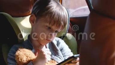 阳光明媚的一天，4岁至6岁快乐的白人男孩在<strong>儿童安全</strong>座椅上使用智能手机，带着玩具
