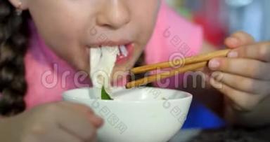 可爱的小孩子正坐在一张桌子旁吃他的面条，宝宝心甘情愿地吃。 小女孩吃面条