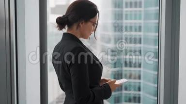 有智能手机的商人肖像。 穿商务服的女人站在一扇大<strong>窗</strong>户旁<strong>边</strong>，<strong>背景</strong>是