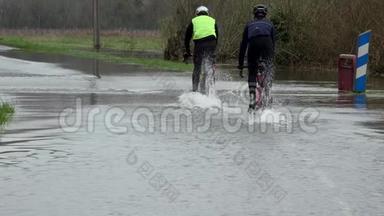 骑自行车的人骑在一条被洪水淹没的道路上，水在道路上，道路被河流的溢流淹没