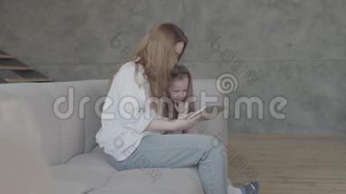一位<strong>年轻</strong>的母亲和小女儿，长发一起坐在客厅的沙发上，用平板电脑。 这<strong>就是</strong>
