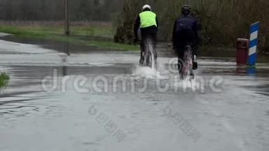 骑自行车的人骑在一条被洪水淹没的道路上，水在道路上，道路被河流的溢流淹没