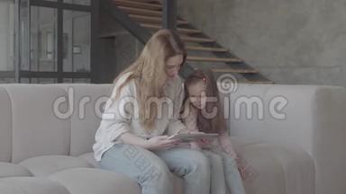 肖像画上漂亮的年轻母亲和她可爱的小女儿正在用平板电脑，微笑着坐在<strong>大沙发</strong>上