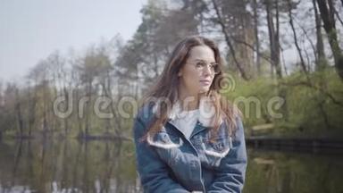 一个优雅的年轻女人戴着太阳镜和一件牛仔夹克漂浮在湖面或河流上的船上的肖像。 美丽美丽