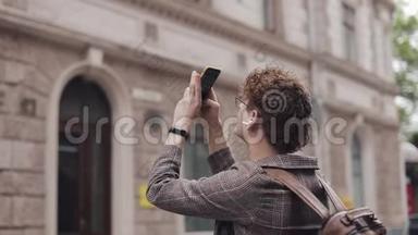 一个戴眼镜的家伙在欧洲旅行时用他的相机手机拍照。 游客用相机拍照