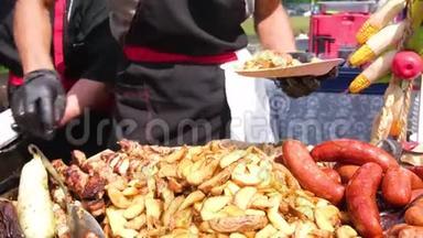 街头美食节。 一位穿着黑色衣服和手套的厨师把油炸食品铺在盘子上。 土豆，烤香肠，肉