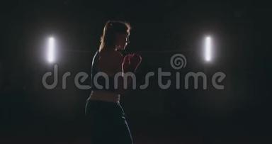 一位身穿红色绷带、蓝色t恤的漂亮运动拳手女子正在与一个正在练习拳击的影子搏斗