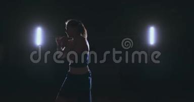 一位身穿红色绷带、蓝色t恤的漂亮运动拳手女子正在与一个正在练习拳击的影子搏斗