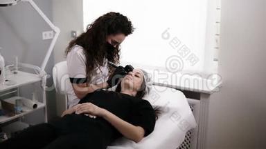 美容师正在为美容院的一位女士画眉毛的形状或用针矫正眉毛。 专业人员
