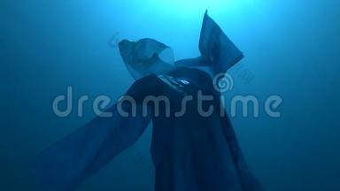 蓝色塑料雨衣作为幽灵慢慢漂浮在蓝色的水中。 海底塑料污染海洋