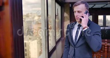 一个穿西装的年轻人站在办公室的窗户附近，打电话，挂断电话，高兴起来。 满意