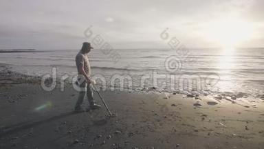 人类正在海滩上遛狗，手持探测器在日出时在海岸线上的沙滩上发现金属。