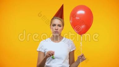 悲伤的成年女人拿着气球吹着噪音制造者，生日<strong>聚会</strong>上心情<strong>不</strong>好