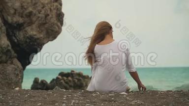 美丽的女孩从后面带着美丽的金发，在风景如画的背景下把鹅卵石扔进水里