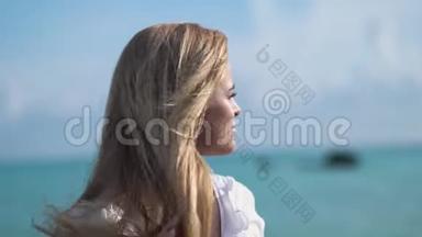一位金发女郎穿着一件白色上衣站在海边或大海上，凝视着大海的近景