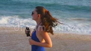 穿着泳衣在海边跑步和听音乐的年轻女子。 女孩沿着海边慢跑。 女<strong>运动</strong>员