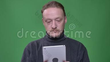 身着灰色套头衫的金发养老金领取者专心地看着平板电脑，在绿色背景上赞许地点头。
