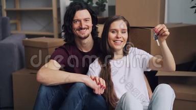 慢镜头肖像幸福夫妇拿着<strong>钥匙</strong>坐<strong>在</strong>新公寓的<strong>地板上</strong>
