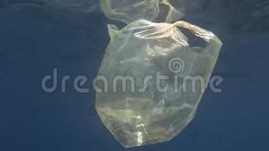 塑料污染，蓝色水中黄色塑料袋。 废弃的塑料袋在阳光下慢慢地漂浮在蓝色的水面下