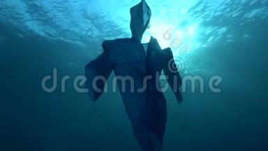 蓝色塑料雨衣作为幽灵慢慢漂浮在蓝色的水中。 海洋的水下塑料污染。