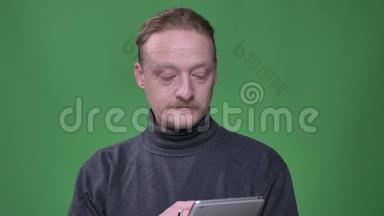 穿灰色<strong>套头衫</strong>的金发养老金领取者专心致志地工作在平板电脑上，并在绿色背景上展示了它的蓝色屏幕。