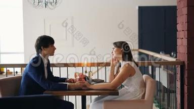 快乐的年轻人女孩和男人正在说着，手捧着鲜花、蜡烛和香槟，坐在桌子上