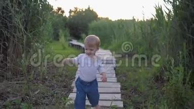 美丽漂亮的小男孩光着脚在高高的<strong>芦苇丛</strong>中的露天木桥上行走