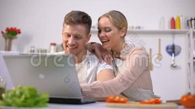 年轻夫妇在网站上寻找食物食谱，笑着，厨房新手