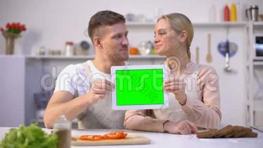 年轻的微笑夫妇展示绿色屏幕平板电脑，烹饪<strong>课程模板</strong>