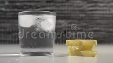 冰块在黑白背景的雾玻璃中随水移动。 在桌子上躺着几片柠檬