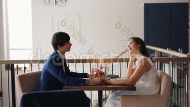 幸福的一对年轻的男女正在谈论，手牵着手坐在餐厅约会。 人们穿着
