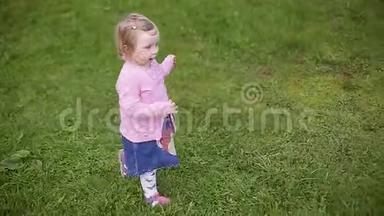 小二岁美丽的金发女孩穿过绿草，慢动作视频。