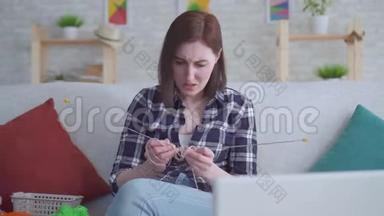 女人坐在笔记本电脑前，看一个关于编织的视频教程，它不起作用
